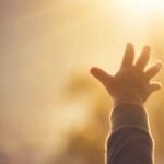 A child's hand reaching toward warm, golden sunlight.