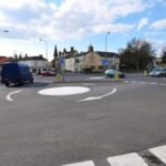 a UK road junction with two small flat painted mini-roundabout circles connected by a short two-way link road, with cars navigating both.