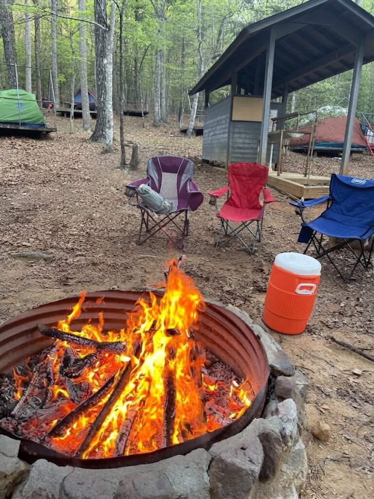 Campfire burning beside folding chairs, tents, and camping platforms at Woodruff Scout Camp.